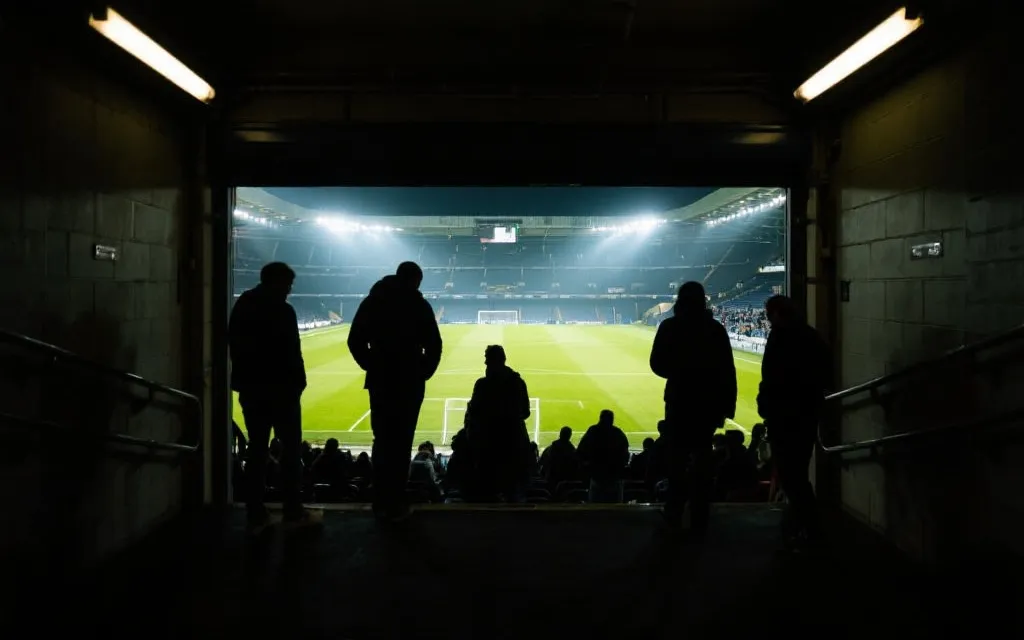夜幕下的球场看台与灯光，球迷在通道中寻找座位的沉浸式体验